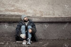 Poor homeless man sitting near wall on street. Space for text